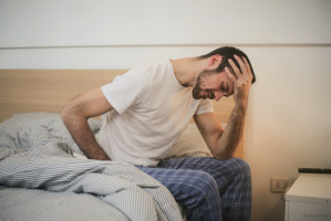 Mann sitzt auf dem Bett mit der Hand am Kopf